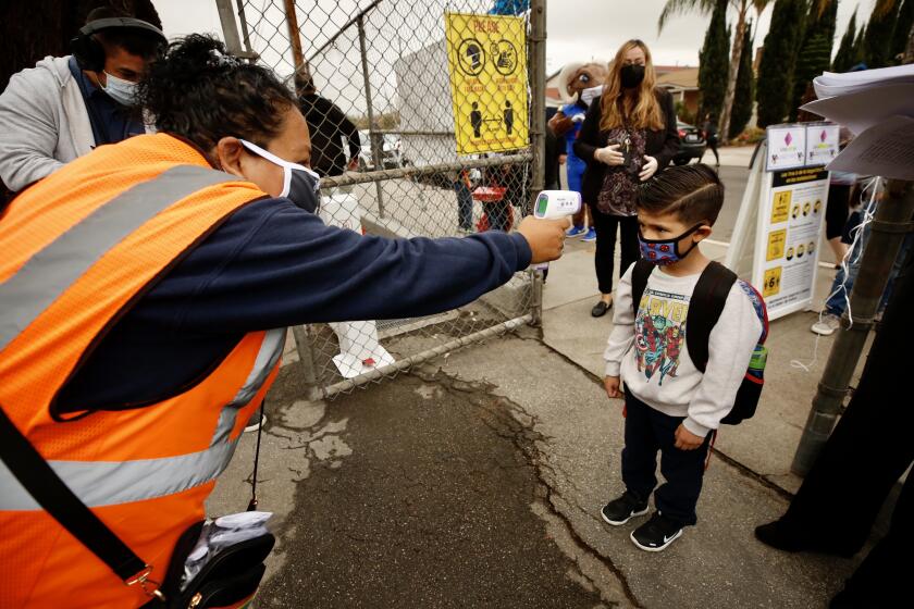 LOS ANGELES CA APRIL 13, 2021 - Kindergarten student Franky Cervantes has temperature checked by school supervisors aide Selena Aguirre before entering Heliotrope Avenue Elementary School for first day of in-class instruction for Kindergarten and first grade students at LAUSD schools, Tuesday morning, April 13, 2021. (Al Seib / Los Angeles Times)