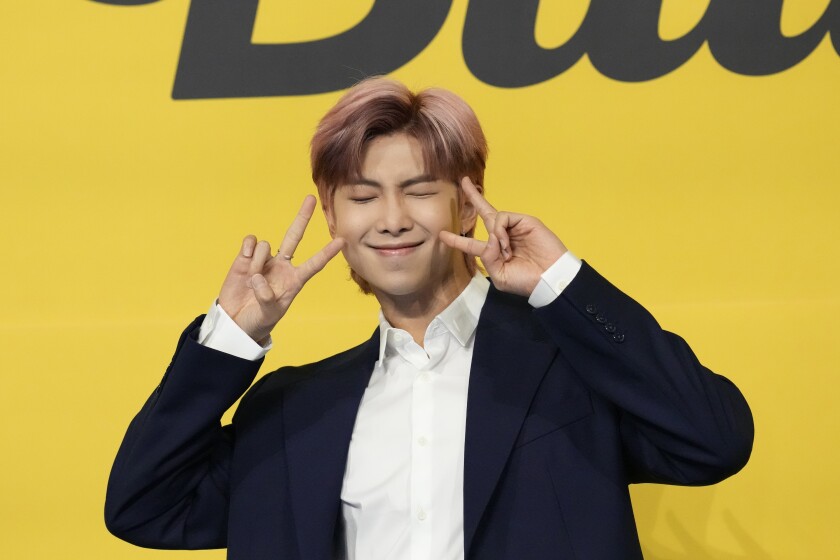 A man with short pink hair throwing up peace signs in a dark blue suit