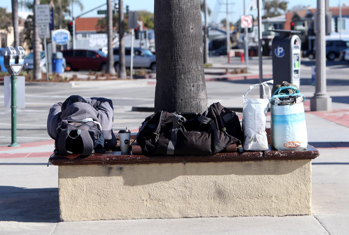 A homeless man sleeps with his belongings packed in bags next to him near the Newport Pier.