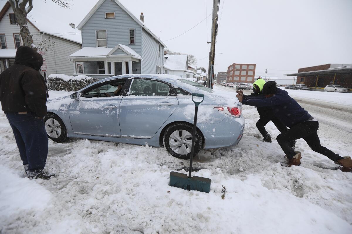 Dwight Green stands nearby as Coty Paige and Cornelius McCaley push a car that got stuck in the snow in Rochester, N.Y., on Tuesday.