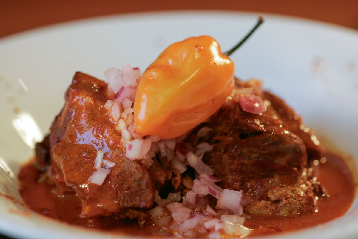 A plate of pork with onions and an orange pepper on top.
