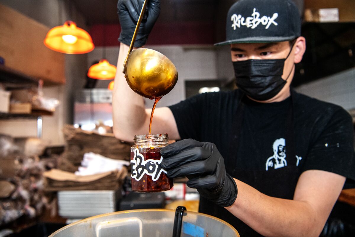 Leo Lee ladles chile oil into a branded glass jar at RiceBox