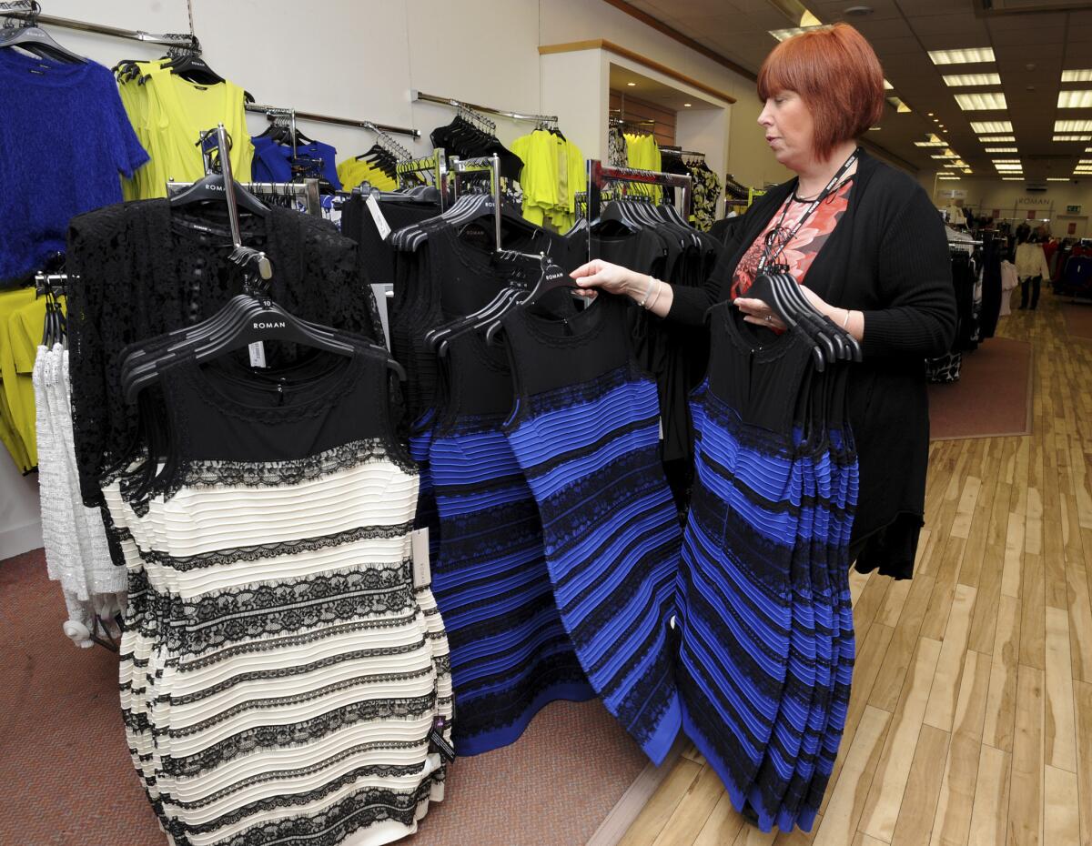 Shop manager Debbie Armstrong places two tone dresses on display at a shop in Lichfield, England, Friday Feb. 27, 2015. It's the dress that's beating the Internet black and blue. Or should that be gold and white? Friends and co-workers worldwide are debating the true hues of a royal blue dress with black lace that, to many an eye, transforms in one photograph into gold and white