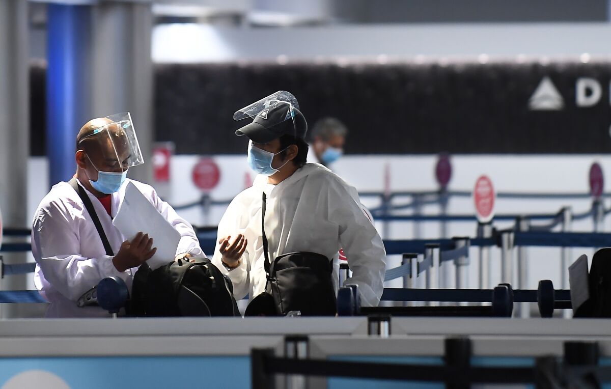 Travelers in face shields, masks and protective clothing talk at a virtually empty LAX.