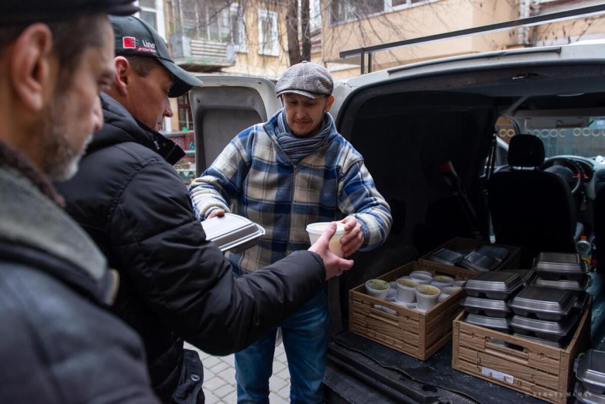 A man outside a vehicle hands out food to a line of people.