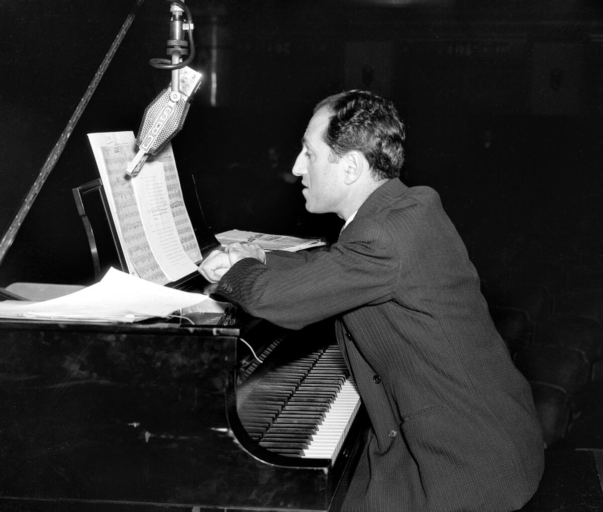 George Gershwin leans over a piano keyboard. 