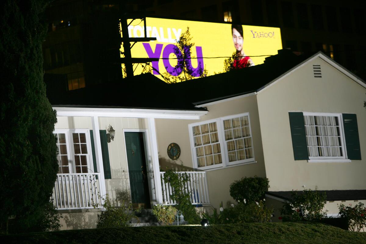 A bright billboard appears behind a house at night.