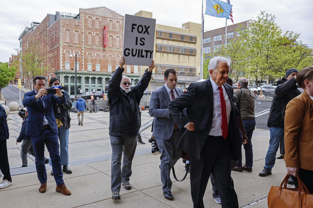 Tailed by a lone demonstrator, the legal team representing Fox News arrives at the courthouse.