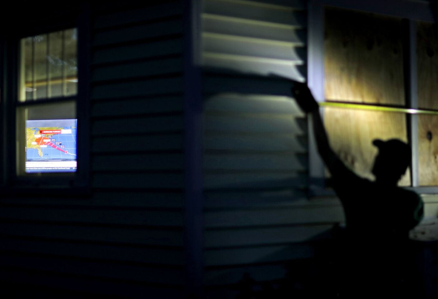 Russell Meadows boards up his neighbors home as a projection of Hurricane Florence is broadcast on a television inside in Morehead City, N.C., Tuesday, Sept. 11, 2018. Florence exploded into a potentially catastrophic hurricane Monday as it closed in on North and South Carolina, carrying winds up to 140 mph (220 kph) and water that could wreak havoc over a wide stretch of the eastern United States later this week.