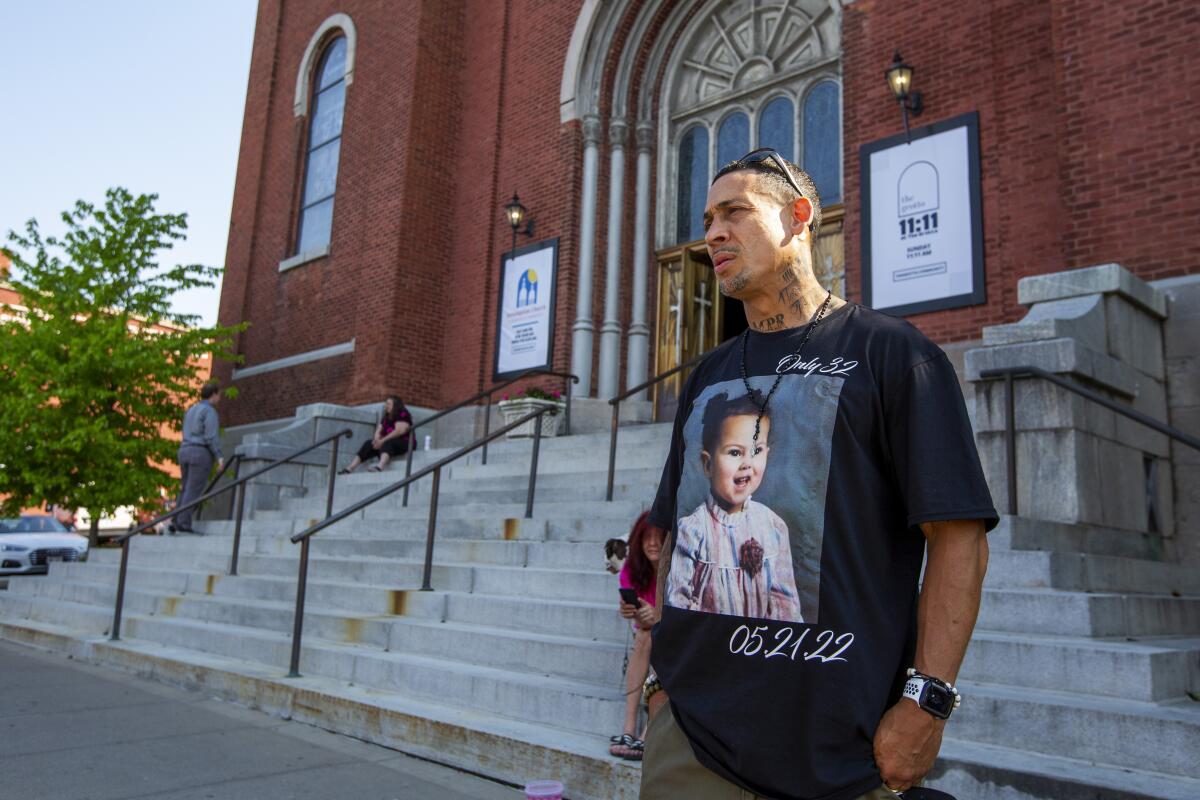 A man wears a T-shirt with a girl's photograph on it before a funeral service.