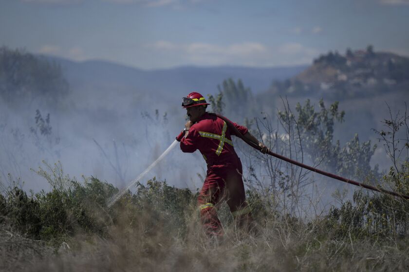 A firefighter directs water on a grass fire on an acreage behind a residential property in Kamloops, British Columbia, Monday, June 5, 2023. No structures were damaged but firefighters had to deal with extremely windy conditions while putting out the blaze. (Darryl Dyck/The Canadian Press via AP)