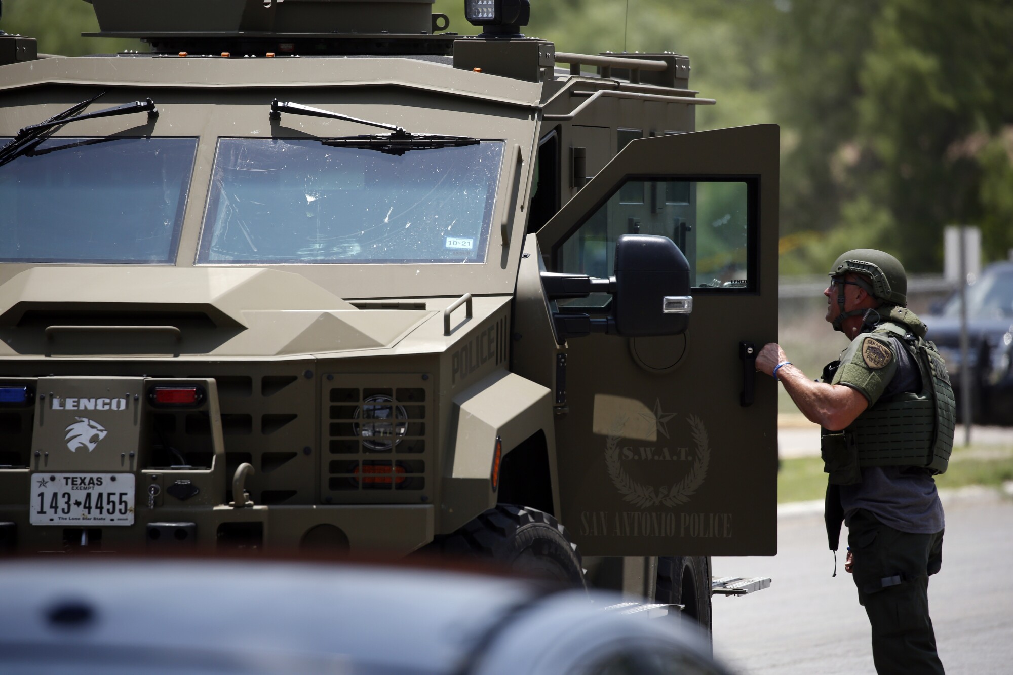 A man in helmet and vest holds the open door of a SWAT police vehicle 