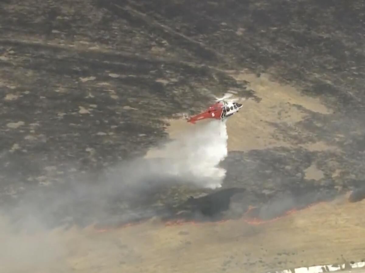 A helicopter drops white spray on a row of flames.