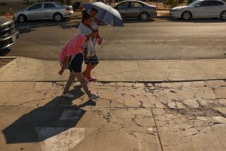 Pacoima, CA - September 06: A family walks by while holding an umbrella and covering their head with a shirt on Friday, Sept. 6, 2024 in Pacoima, CA. (Michael Blackshire / Los Angeles Times)