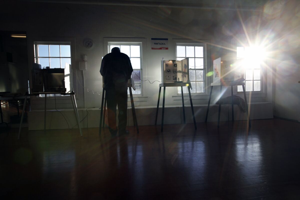 A man seen in shadow stands at a voting booth  