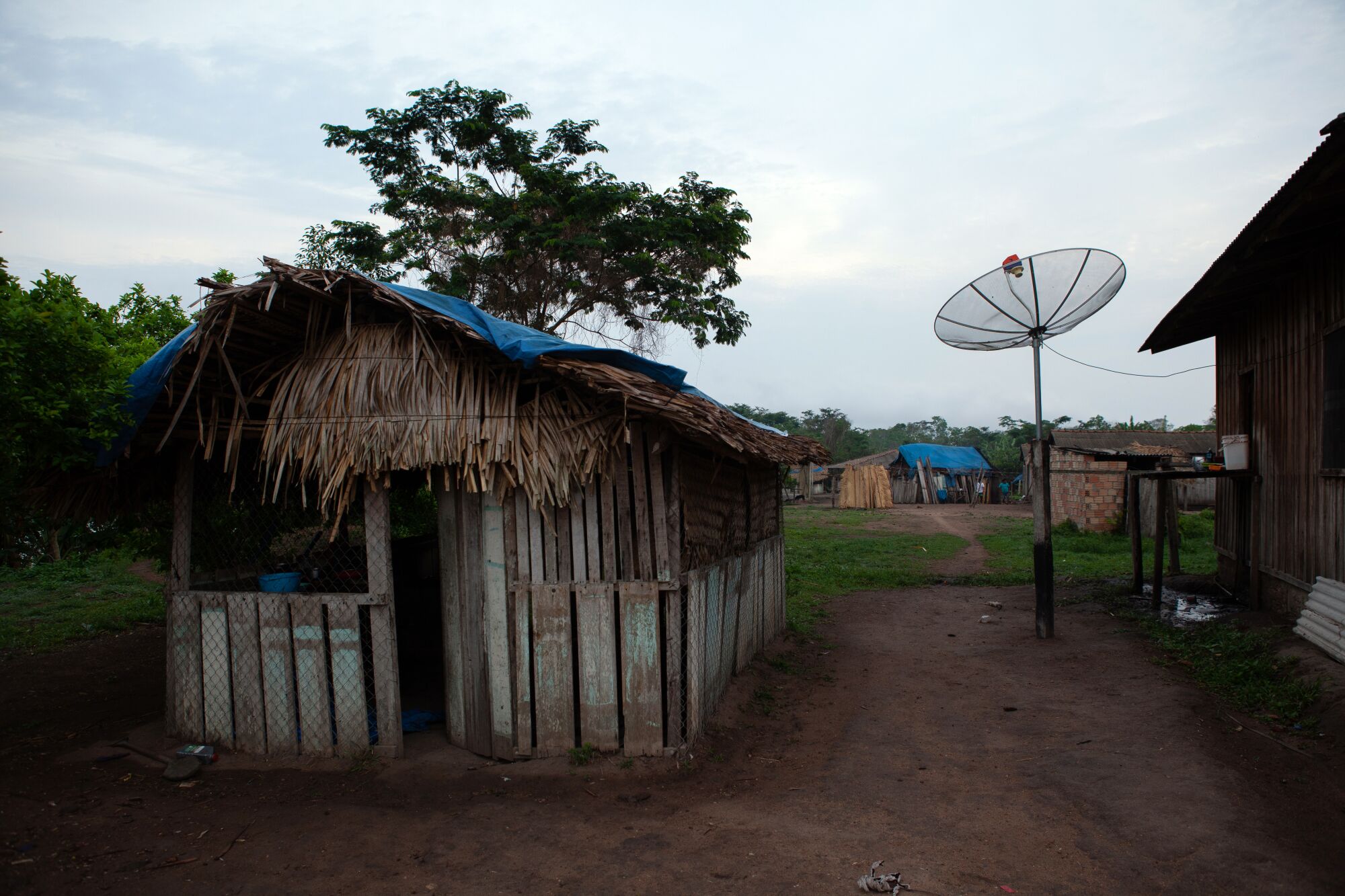 A hutlike home in a village with a large round antenna nearby 