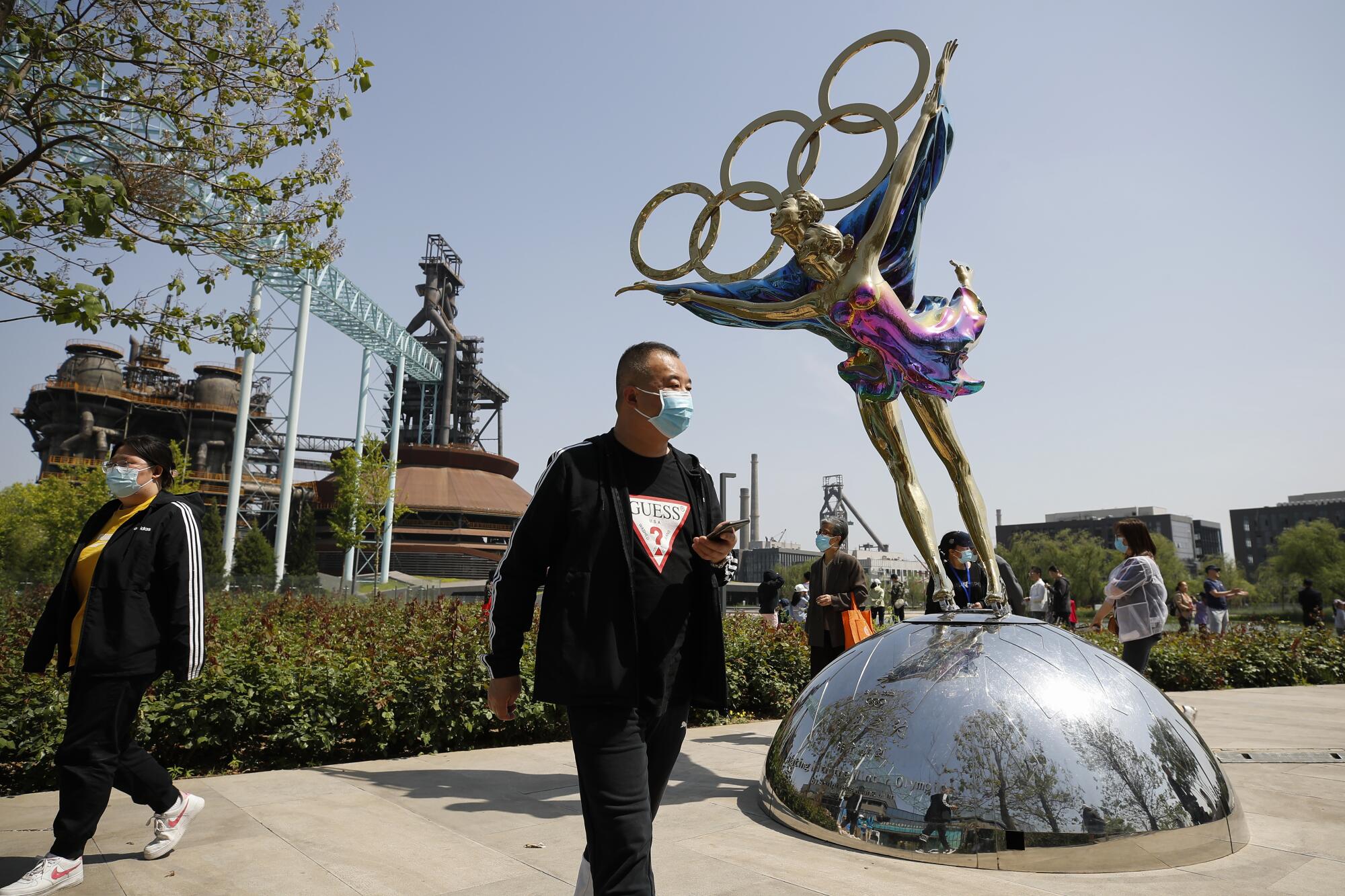 Visitors wearing face masks walk by a statue featuring Winter Olympics figure skating at the Shougang Park in Beijing