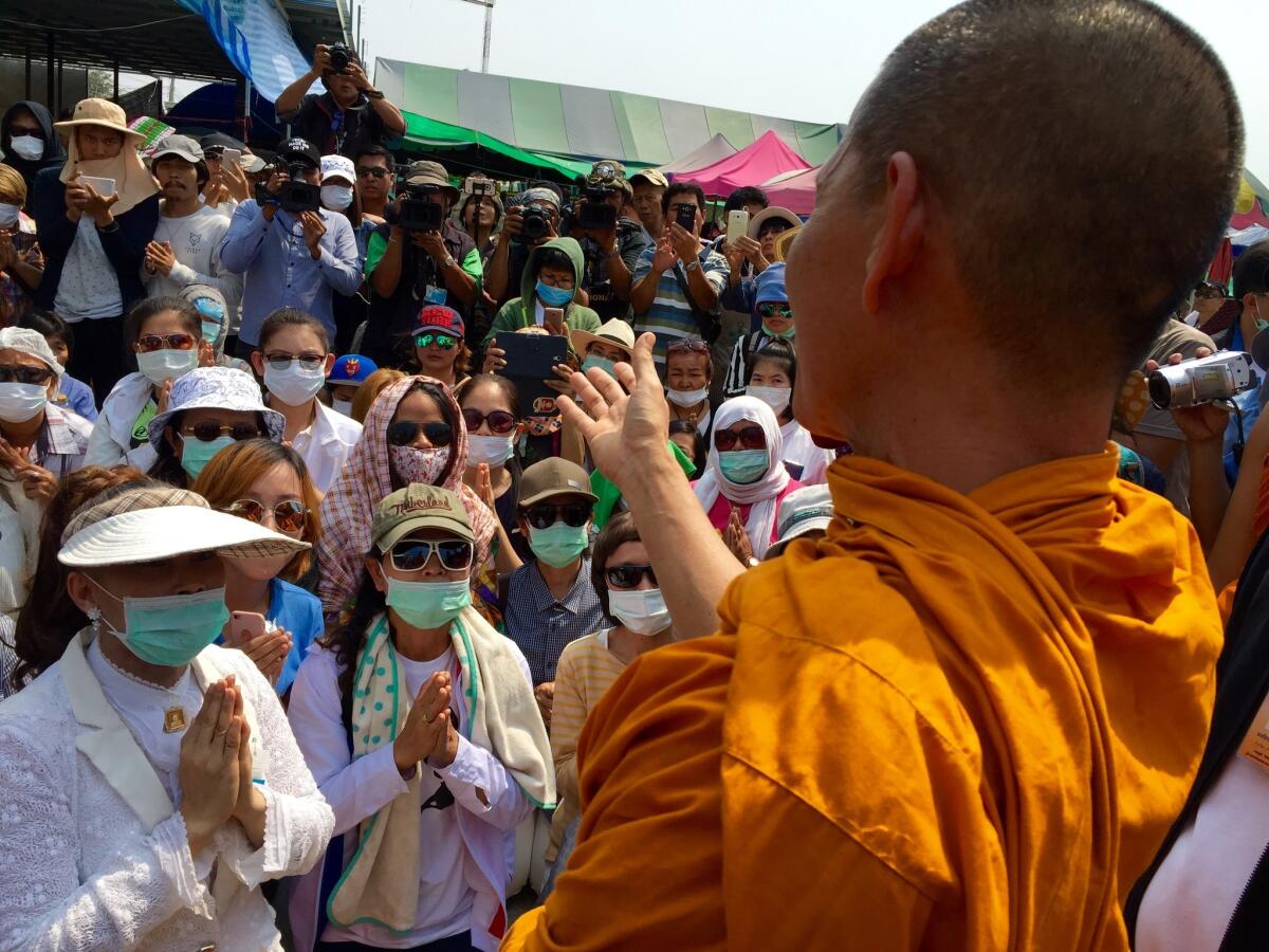 Hands clasped in prayer, followers of the Buddhist Dhammakaya sect meet with a monk outside their temple north of Bangkok, where their spiritual leader is believed to be evading arrest.