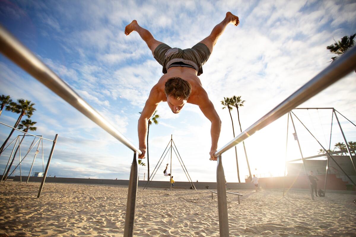 Brian Comstock, 29, does a hand stand on exercise bars at Muscle Beach on Friday.