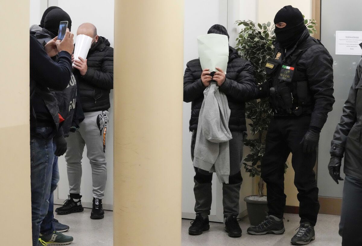 Iraqi suspects Alaa Qasim Rahima, second left and Omar Qasim Rahima, second right, conceal their faces after their arrest by Italian Finance Police, at the Venice barrack, northern Italy, Wednesday, Jan. 19, 2022. Police in Italy and Albania arrested more than 20 people accused of cashing in several hundred million euros to smuggle hundreds of mostly Iraqi and Syrian migrants into the EU from Turkey on rented yachts and other leisure vessels, authorities said Wednesday. (AP Photo/Luca Bruno)