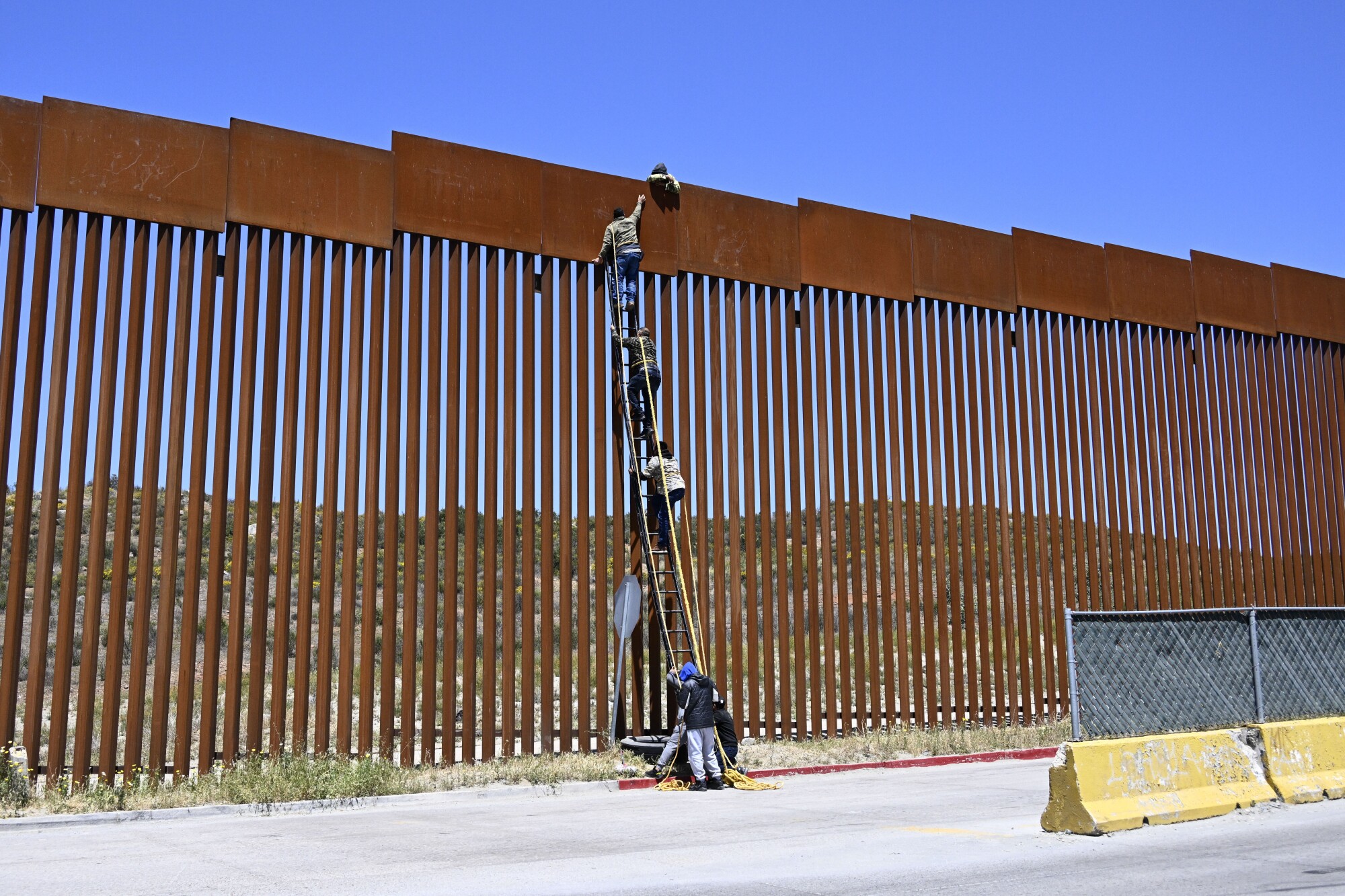 People use a ladder to scale the border fence at the US-Mexico border