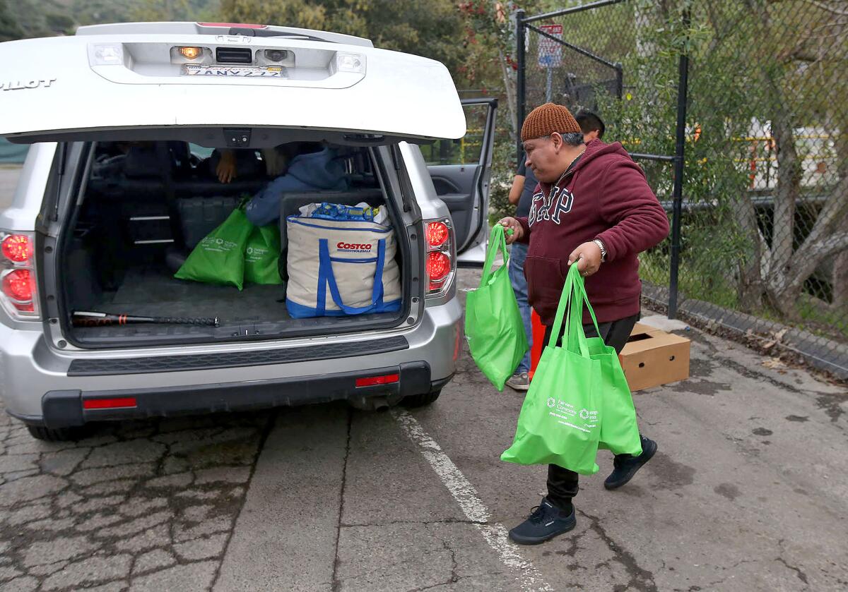Customers pick up groceries during drive-up distribution outside the Laguna Food Pantry on Wednesday. Shoppers normally would go inside the pantry, but it is now serving people outside to follow precautions against the coronavirus.