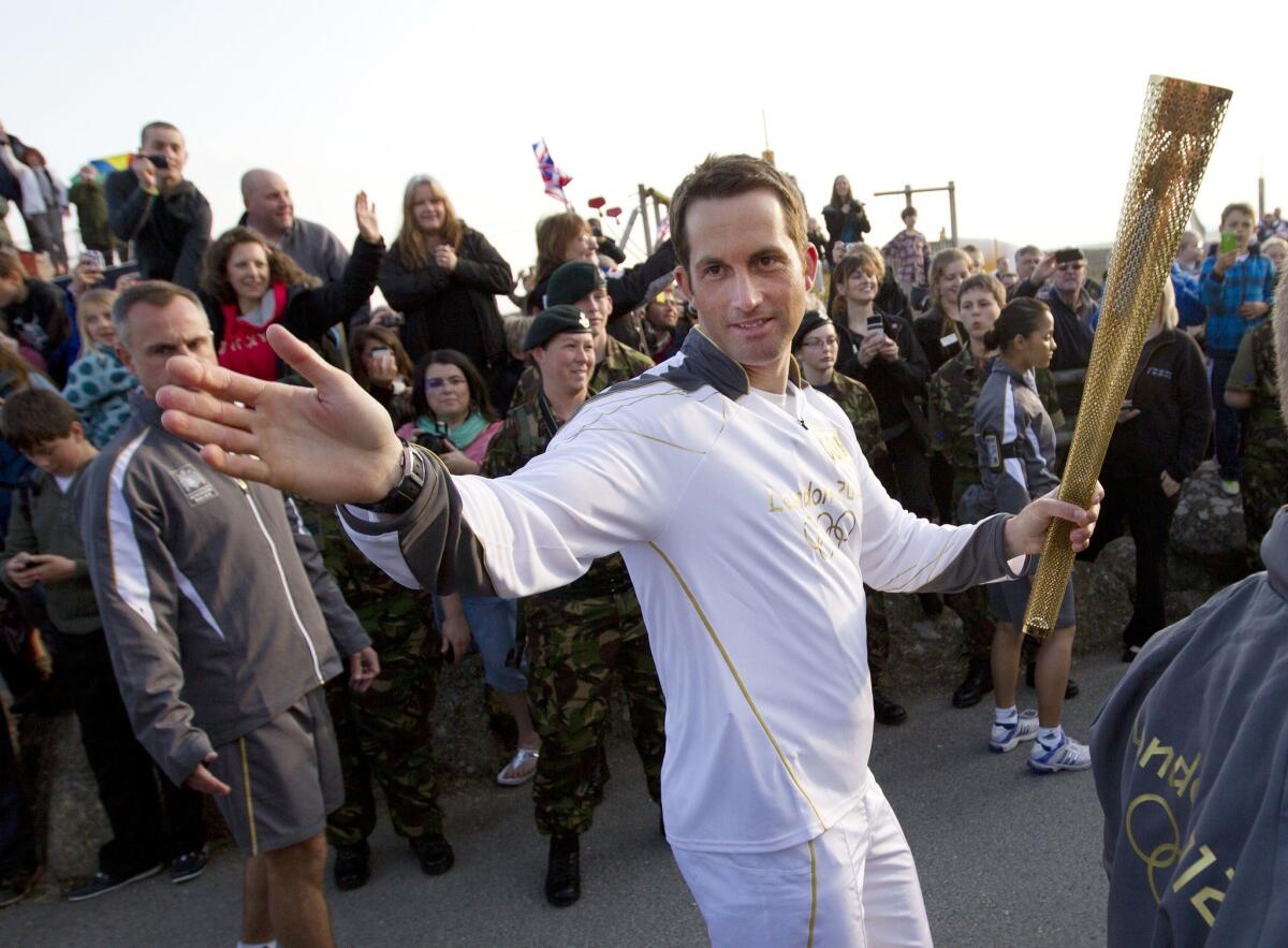 British Olympic sailing hero and three-time gold medalist Ben Ainslie waves to the crowd as he holds the Olympic torch in 2012.