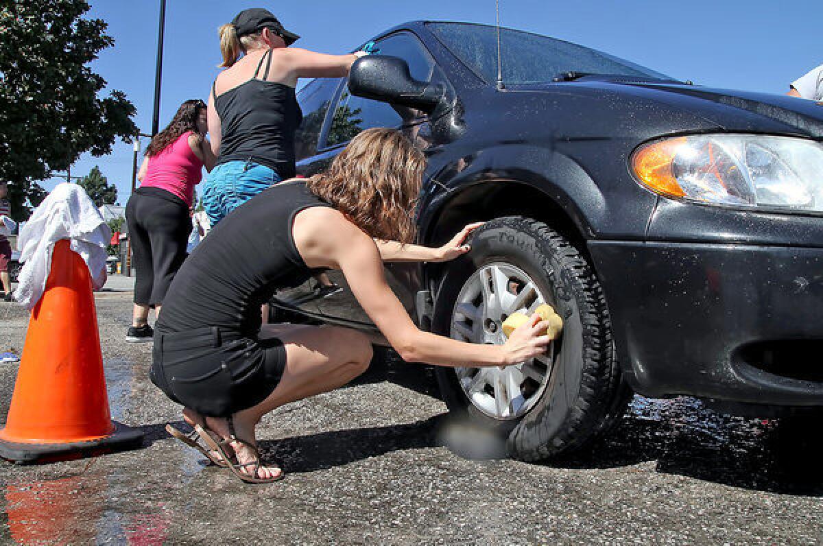 Britini Parish scrubs the tire of a car during a car wash fundraiser last Saturday at Fosters Freeze on Glenoaks Boulevard. Donations were collected for the families of five car crash victims.
