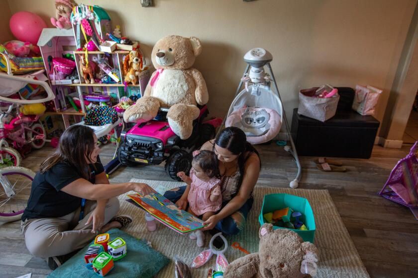 Compton, CA - August 23: Parent coach Alba Mariscal, left, visits mother Ilse Ochoa, left, and ten-month-old baby Brianna de Leon, right, on Wednesday, Aug. 23, 2023, in Compton, CA. Parent coaches go house to house, checking in on these families through the first year of their baby's life. They offer tips and advice, and often just support in what is often a very challenging (though exciting) moment for new parents. But funding for this crucial program is at risk. First 5 is funded through a tobacco tax, and as more and more Californians give up their cigarettes, that funding money is starting to dry up. (Francine Orr / Los Angeles Times)