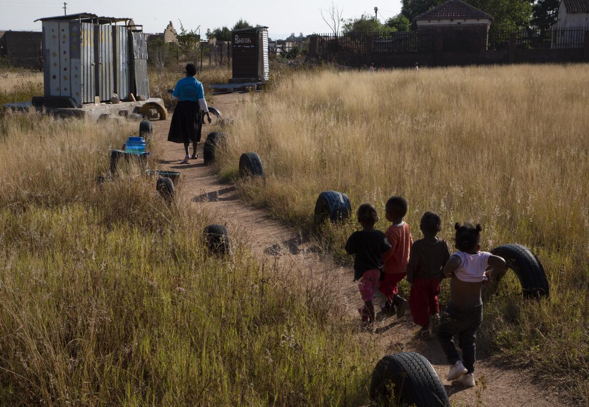 Children follow a school manager toward pit toilets in South Africa.