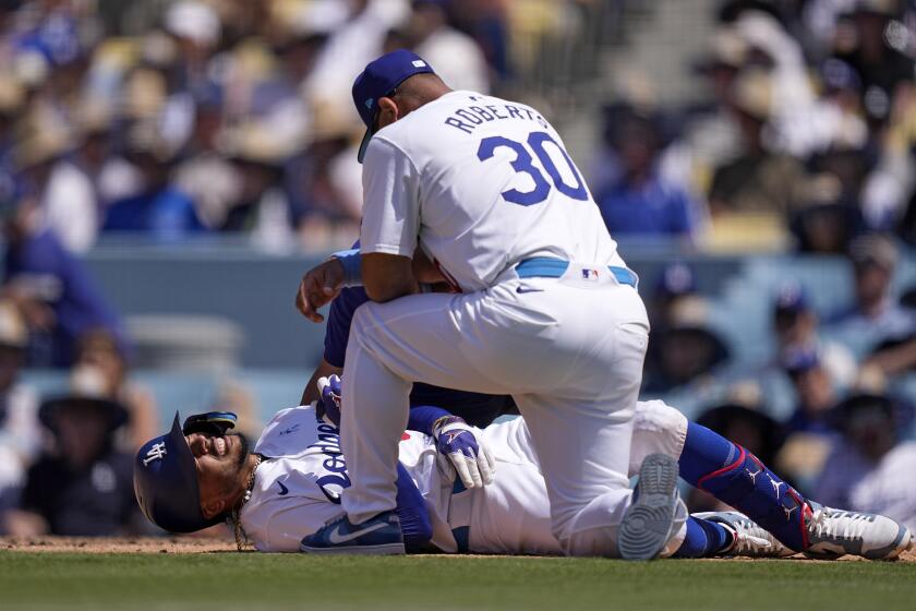 Los Angeles Dodgers' Mookie Betts, left, writhes on the ground after being hit by a pitch.