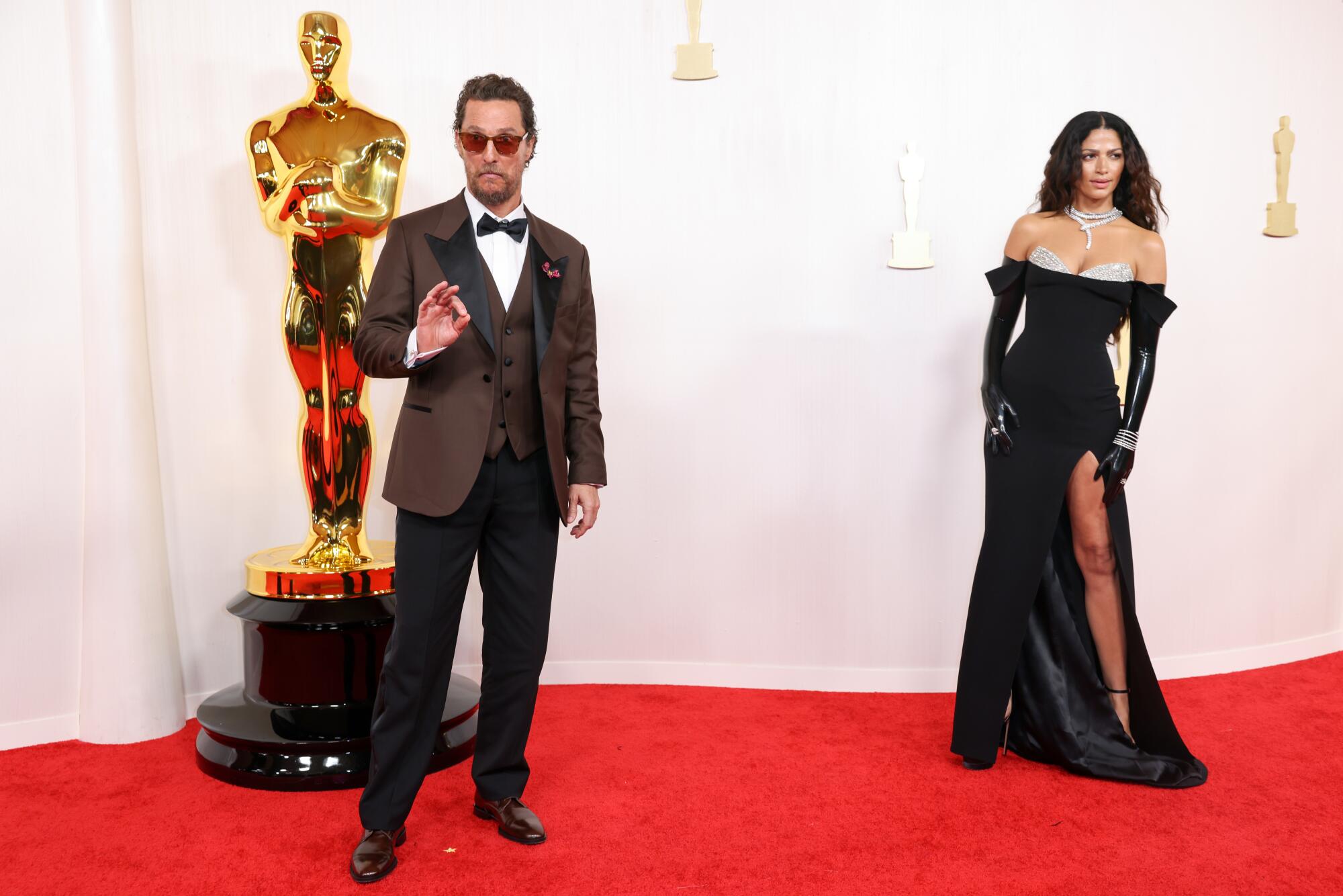 Matthew McConaughey wears a brown jacket, and Camila Alves wears a black gown with opera gloves. 