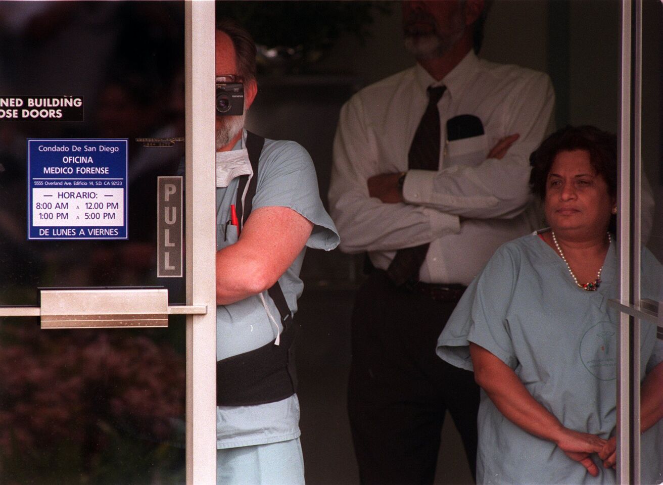 San Diego County Medical Examiner's Office personnel watch and take photographs from the doorway of their office during a news conference on the Heaven's Gate mass suicide in March 1997.
