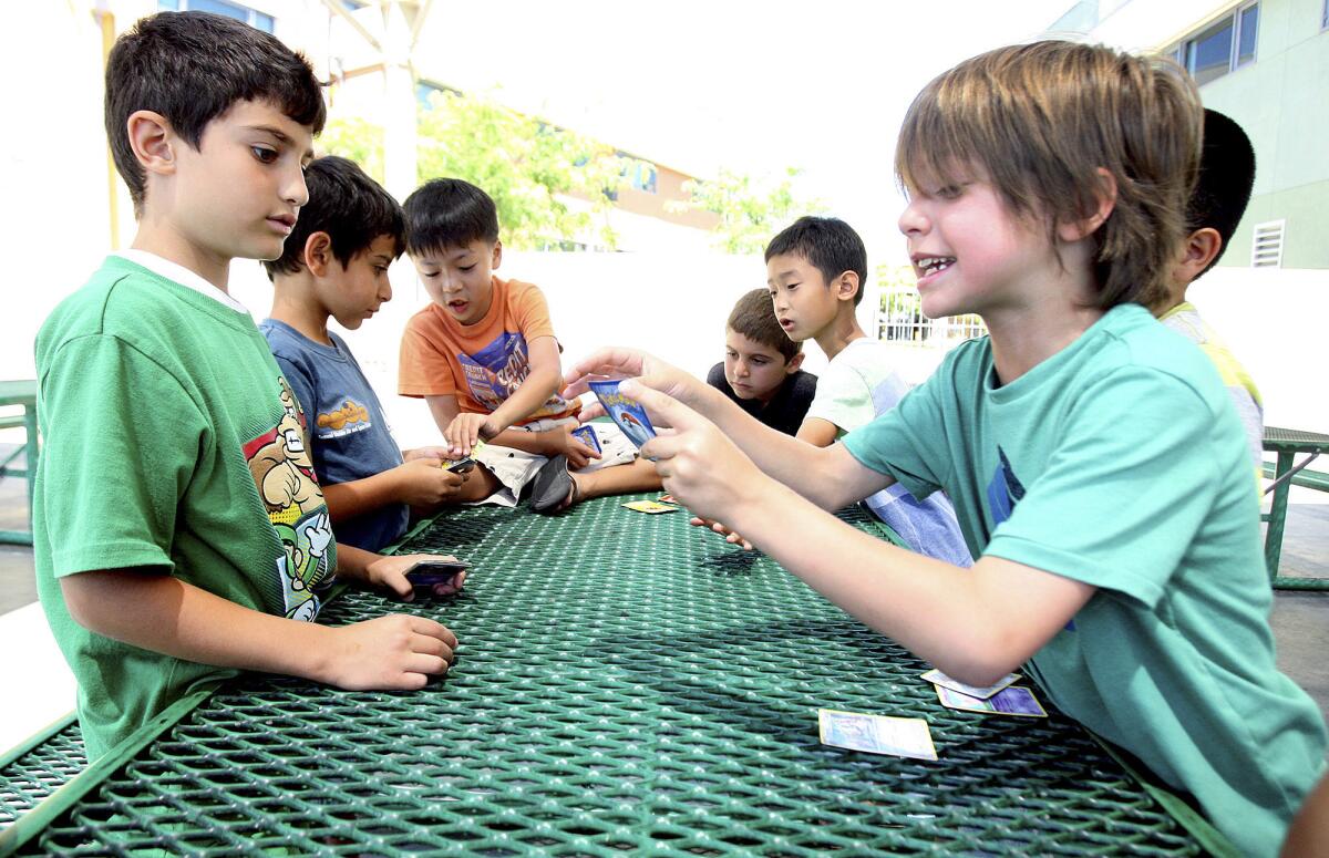 Areg Aslanyan, 7, of Glendale and Adrian Magana-Miller, 7, of Glendale, battle with a group of fellow cardholders on a shaded picnic table in a loud, fast, and competitive Pokemon game at Kool Dayz Camp at the Community Center at Pacific Park in Glendale on Thursday, June 19, 2014.