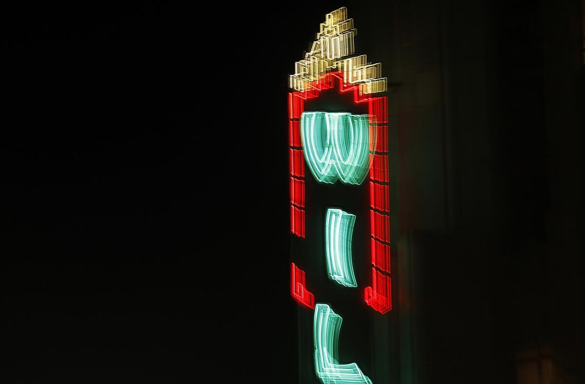 The neon marquee of the Wiltern, a landmark Art Deco theater, glows over the intersection of Wilshire Boulevard and Western Avenue.