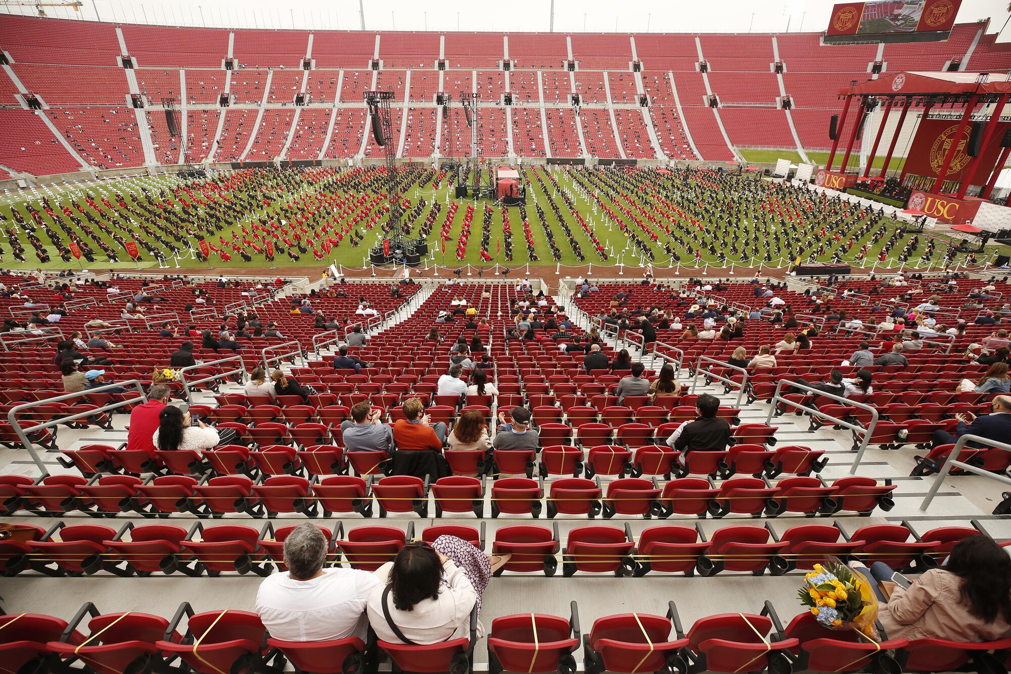 A look down at the Coliseum field filled with students, and people seated in the stands with space between groups