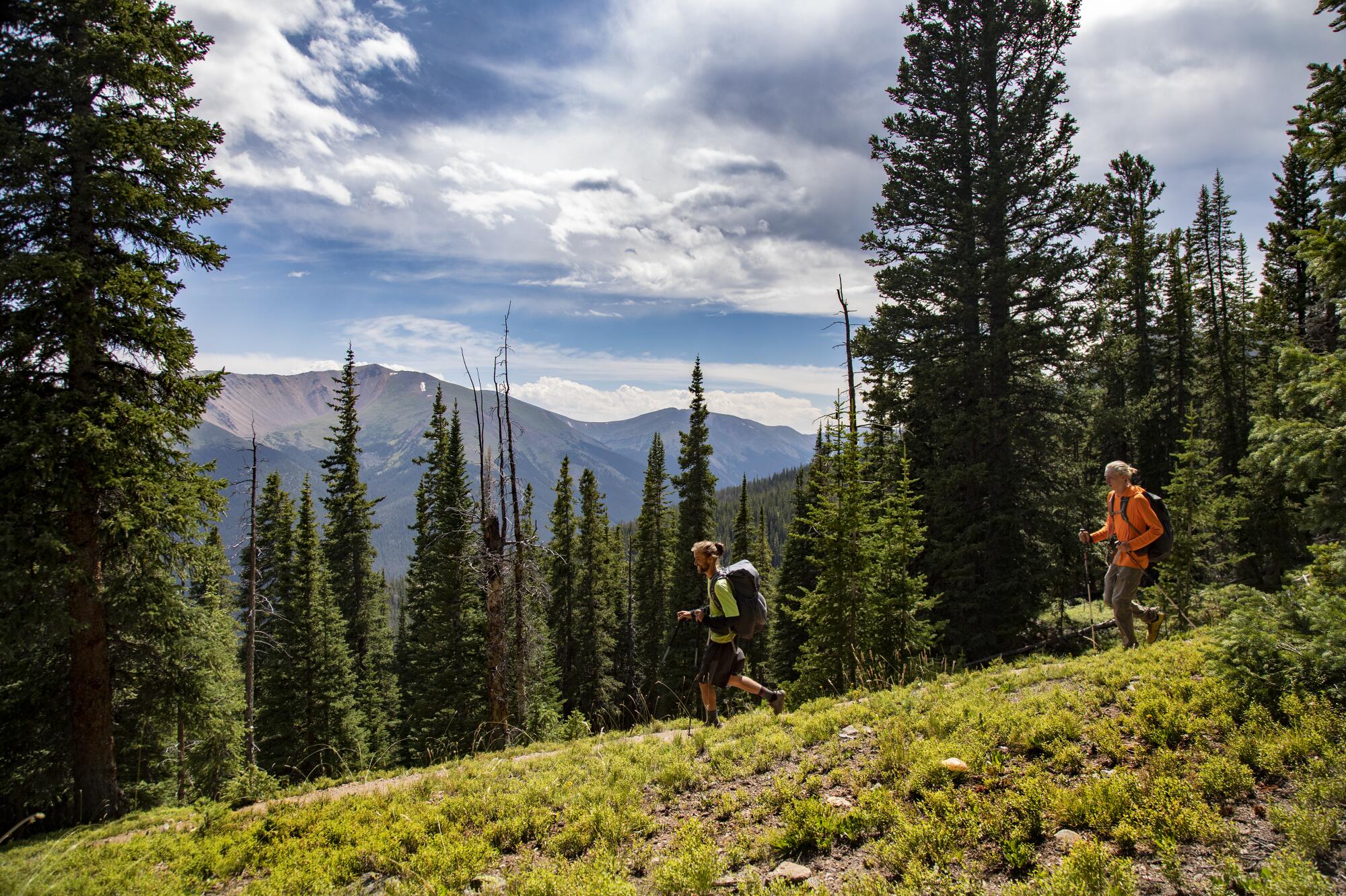 Two men with backpacks hike in mountainous terrain.