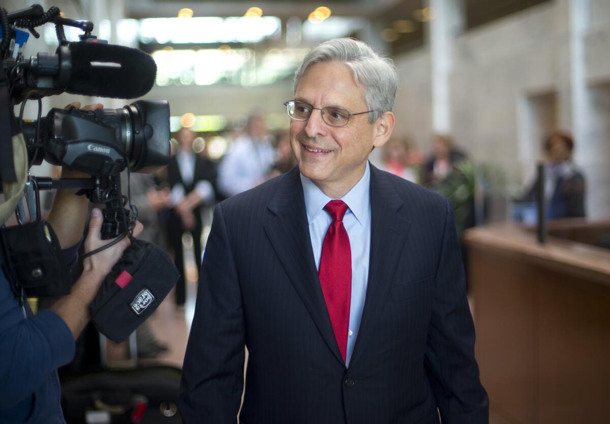 Judge Merrick Garland smiles at reporters holding microphones and cameras.