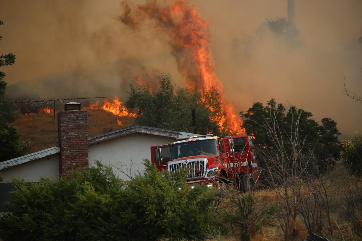 Firetruck parked near a home,  with flames shooting into the sky in the background 