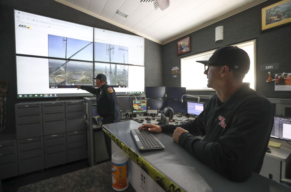 Cal Fire Capt. Kevin Cox points to the screen as he and Capt. Ryan Silva demonstrate the use of wildfire surveillance cameras while in the emergency command center at the Cal Fire San Diego Unit Headquarters on Wednesday.