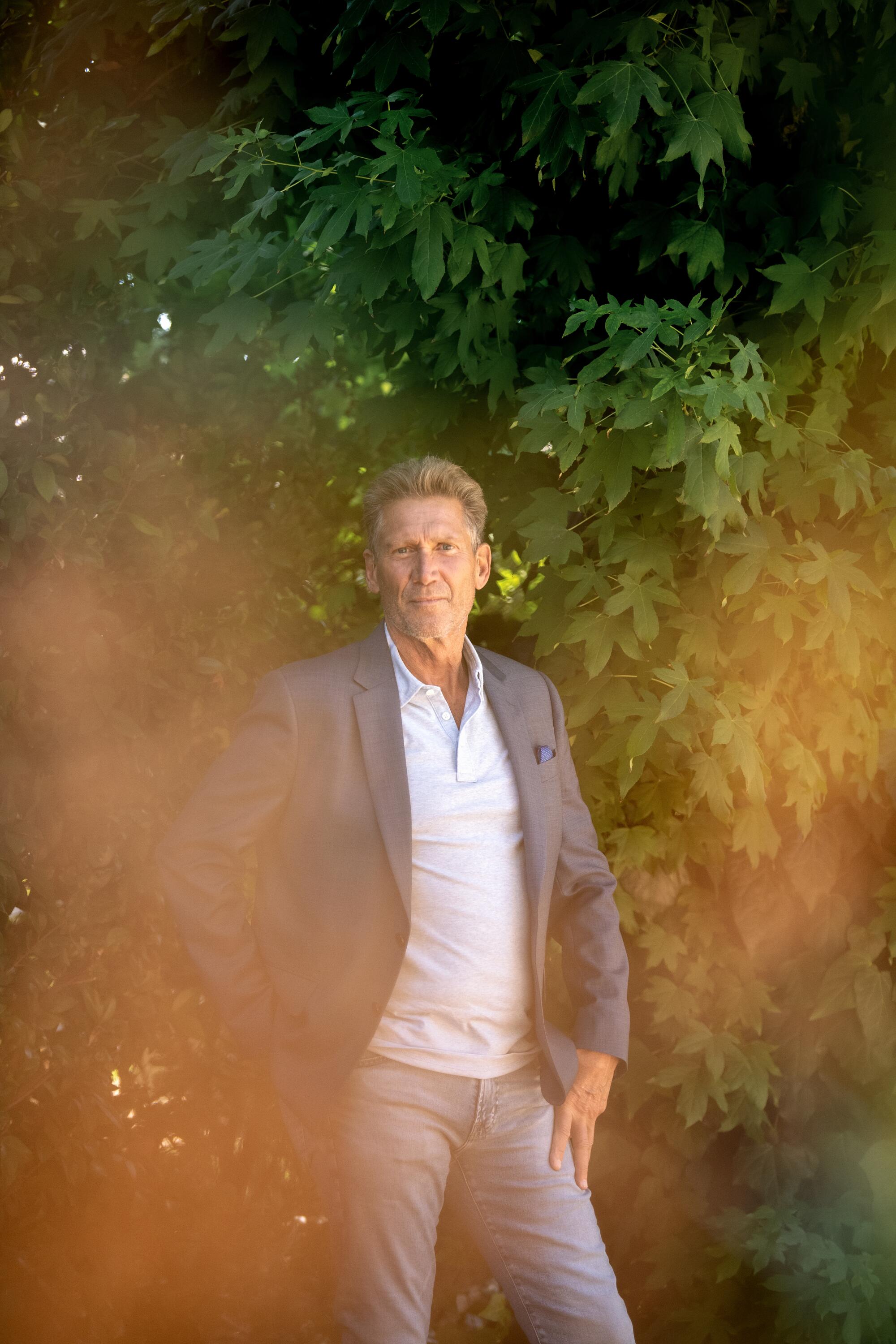 Gerry Turner stands in front of greenery in gray blazer and jeans with his hands near his hips.
