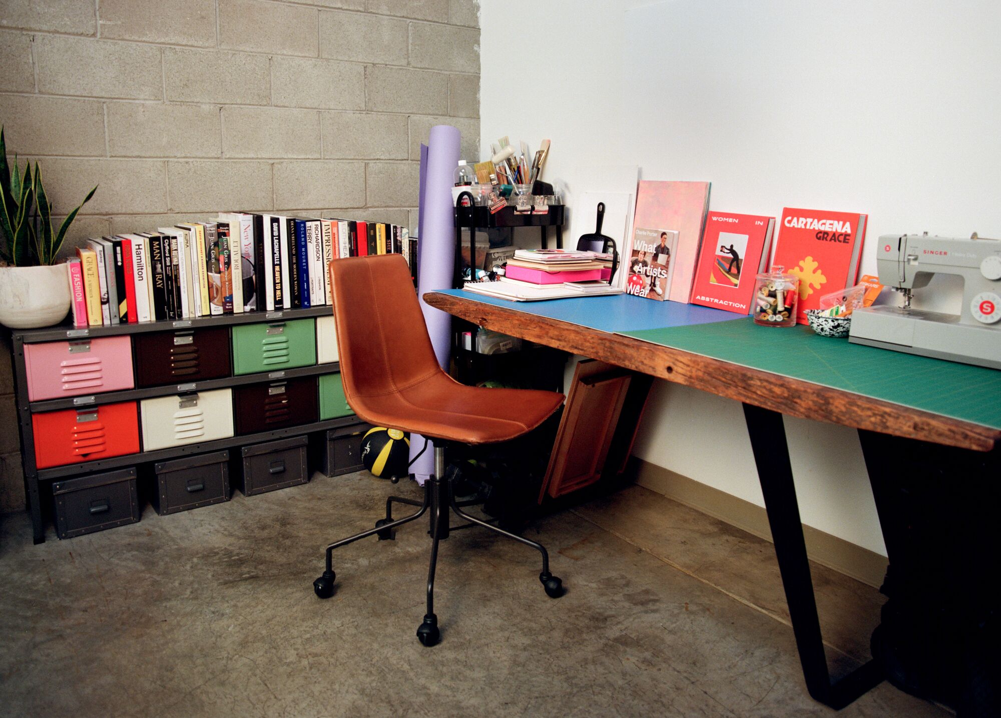 An orange chair at a wooden desk, with a shelf of books and storage boxes behind it.