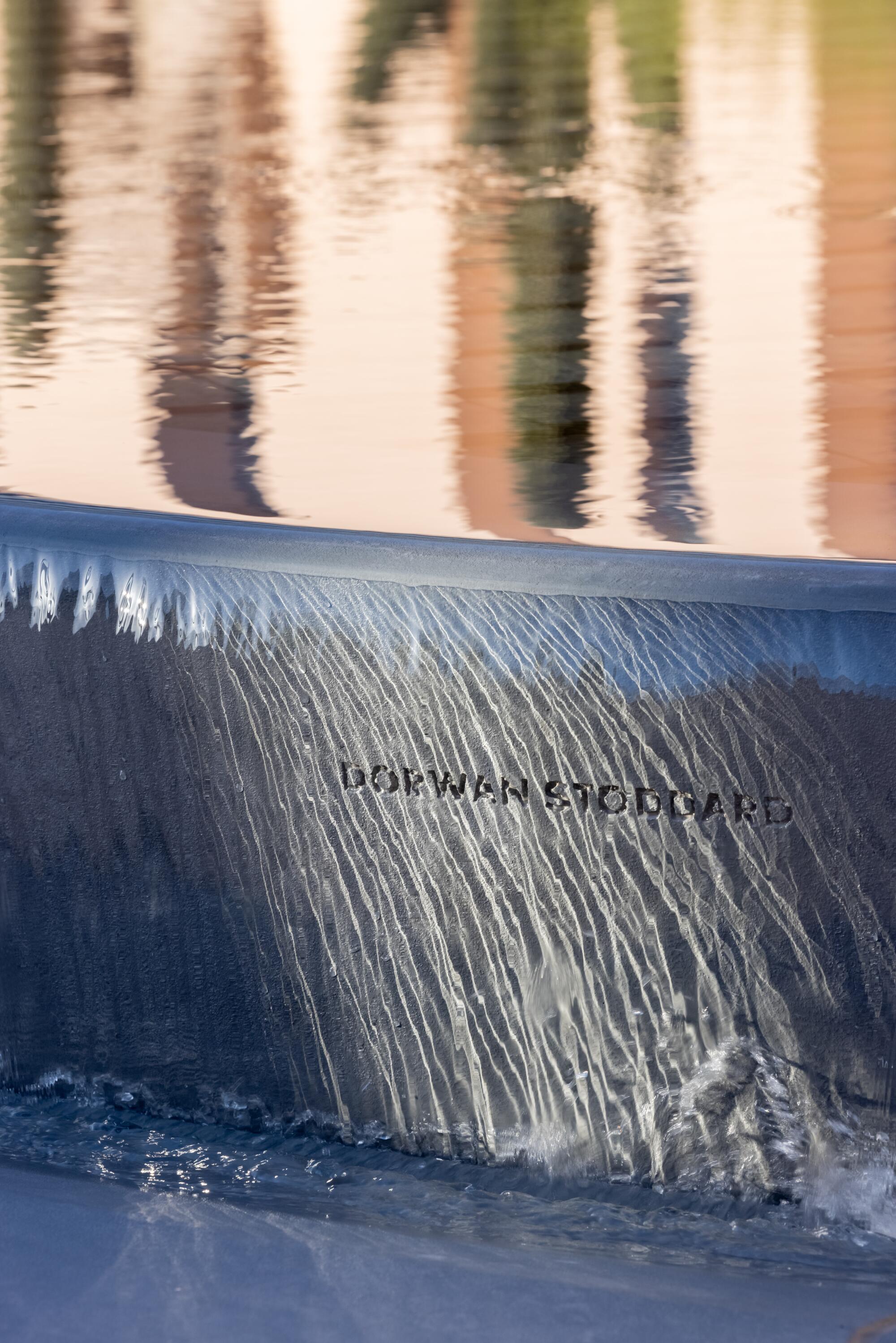 A cascade of water runs over the side of a fountain with the name Dorwan Stoddard embossed.