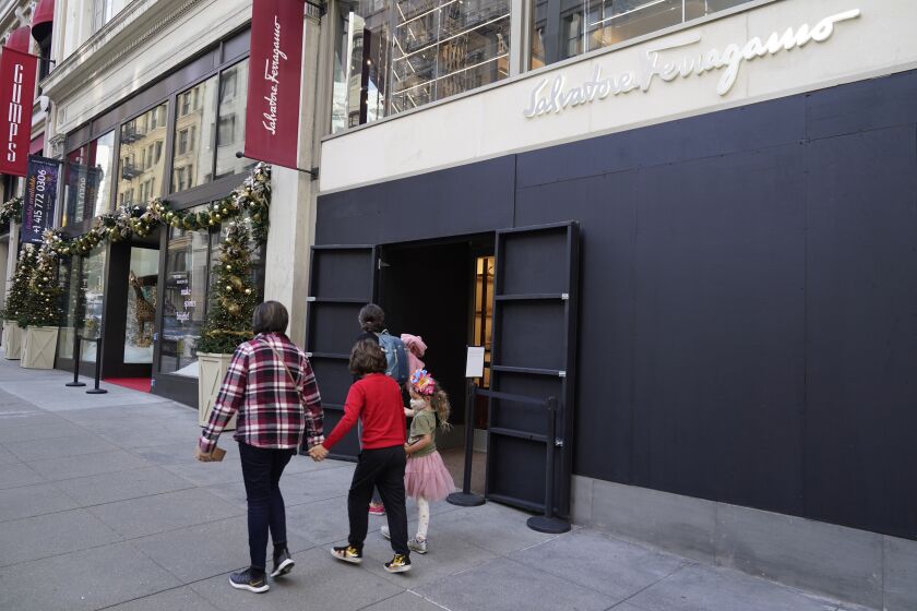 FILE - People walk past a boarded storefront window of a Salvatore Ferragamo store following recent robberies near Union Square in San Francisco, on Dec. 2, 2021. Stung by recent headline-grabbing smash-and-grab robberies at high-end stores, California Gov. Gavin Newsom said Friday, Dec. 17, 2021, that he will seek more than $300 million over three years to boost law enforcement efforts on retail theft, while he also is targeting increasing gun violence. (AP Photo/Eric Risberg, File)