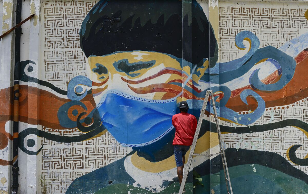 A street artist spray-paints a protective mask over an old mural in Caracas, Venezuela