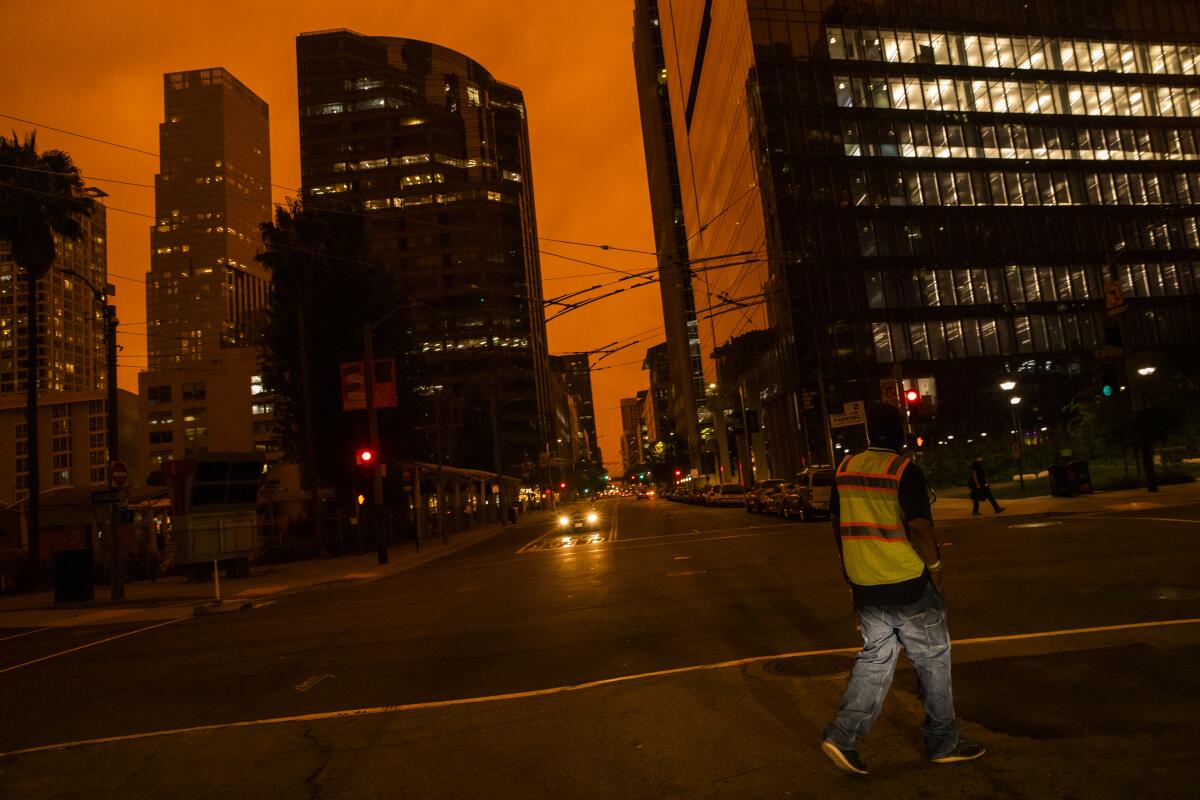 A dark orange, smoky sky is seen between the silhouettes of buildings in San Francisco