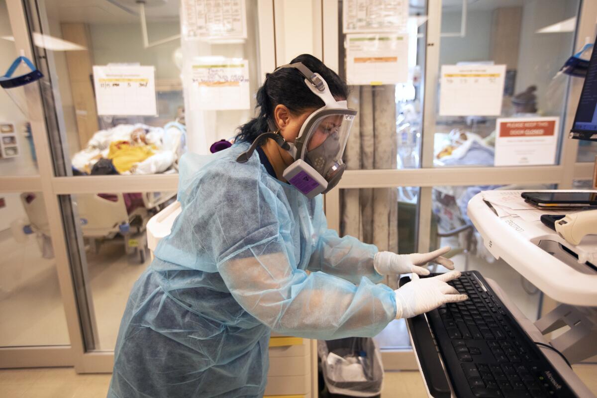 A nurse in a respirator mask, gown and gloves types on a computer keyboard.