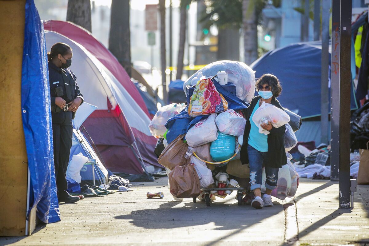 A woman removes her belongings from a homeless encampment as an officer watches.