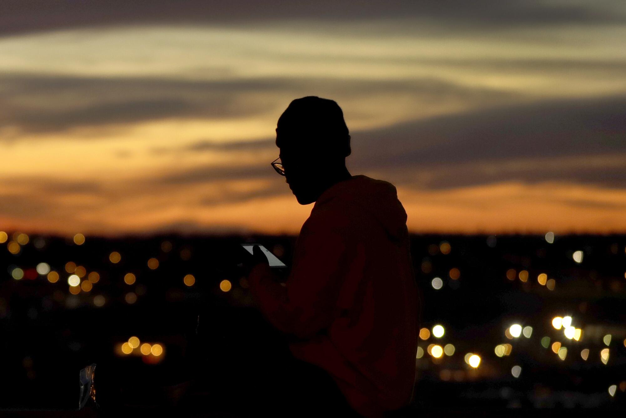 A person looks at a smart device as the sun sets in Kansas City, Mo. Technology has helped enable social distancing.