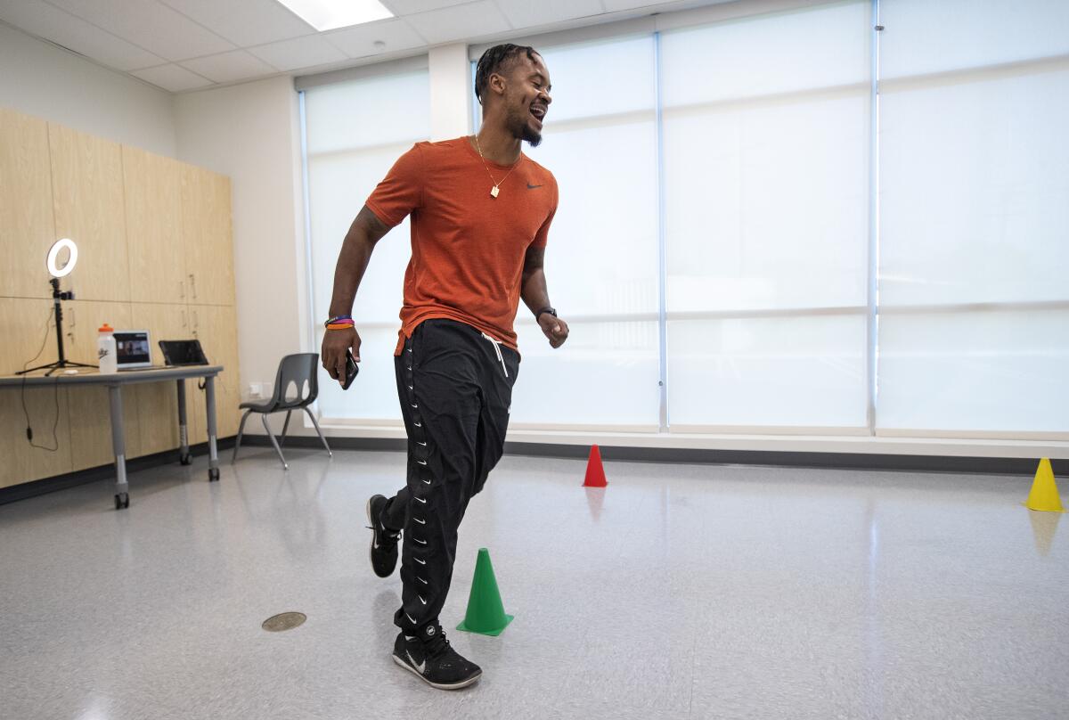 Alfredo Crossman-Chávez Jr. jogs around cones in a classroom while leading an online PE class.